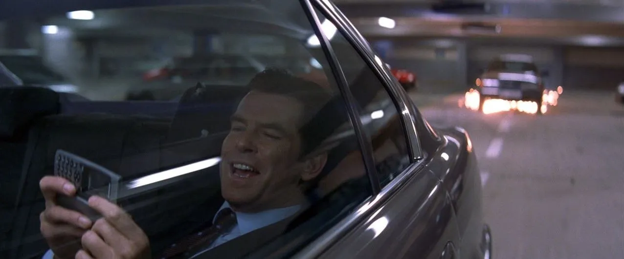 Pierce Brosnan grins while remotely steering his car from the back seat via mobile phone in Tomorrow Never Dies